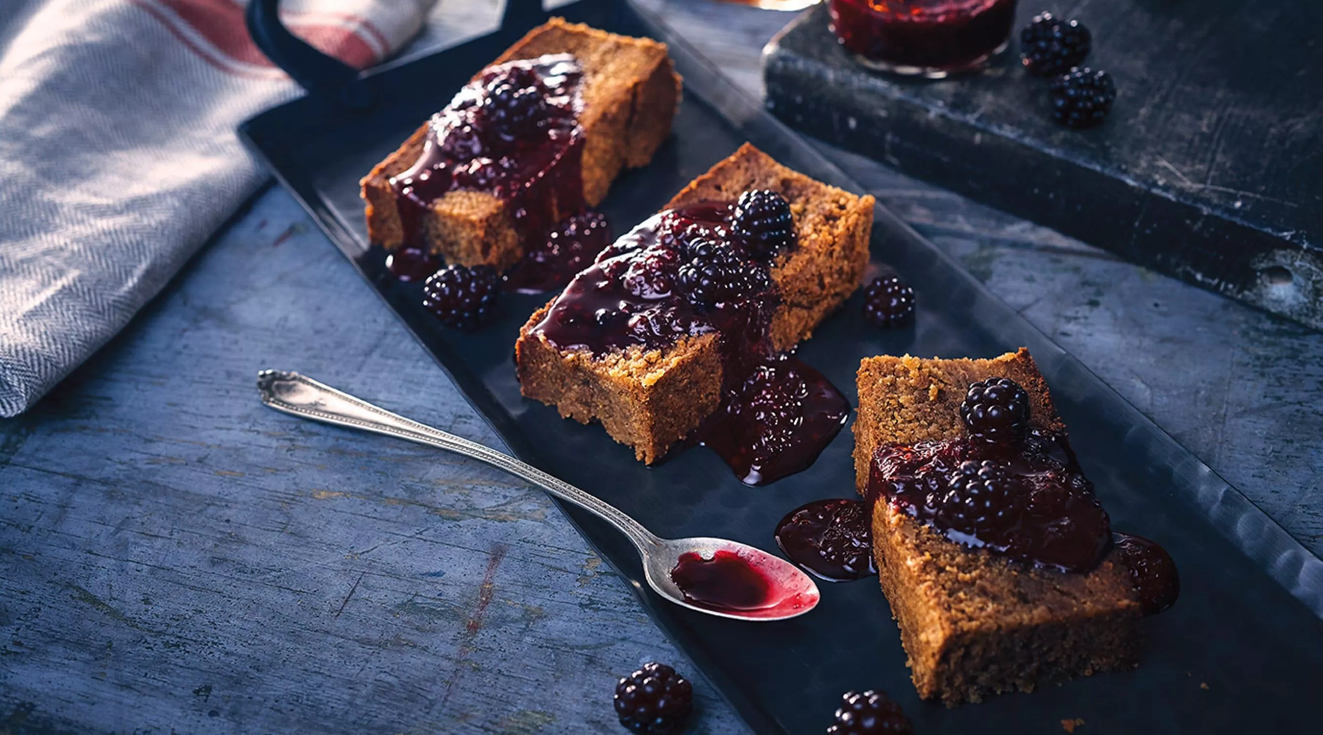 A plate of blondies are presented with fresh blackberries on top and drizzled with blackberry syrup.