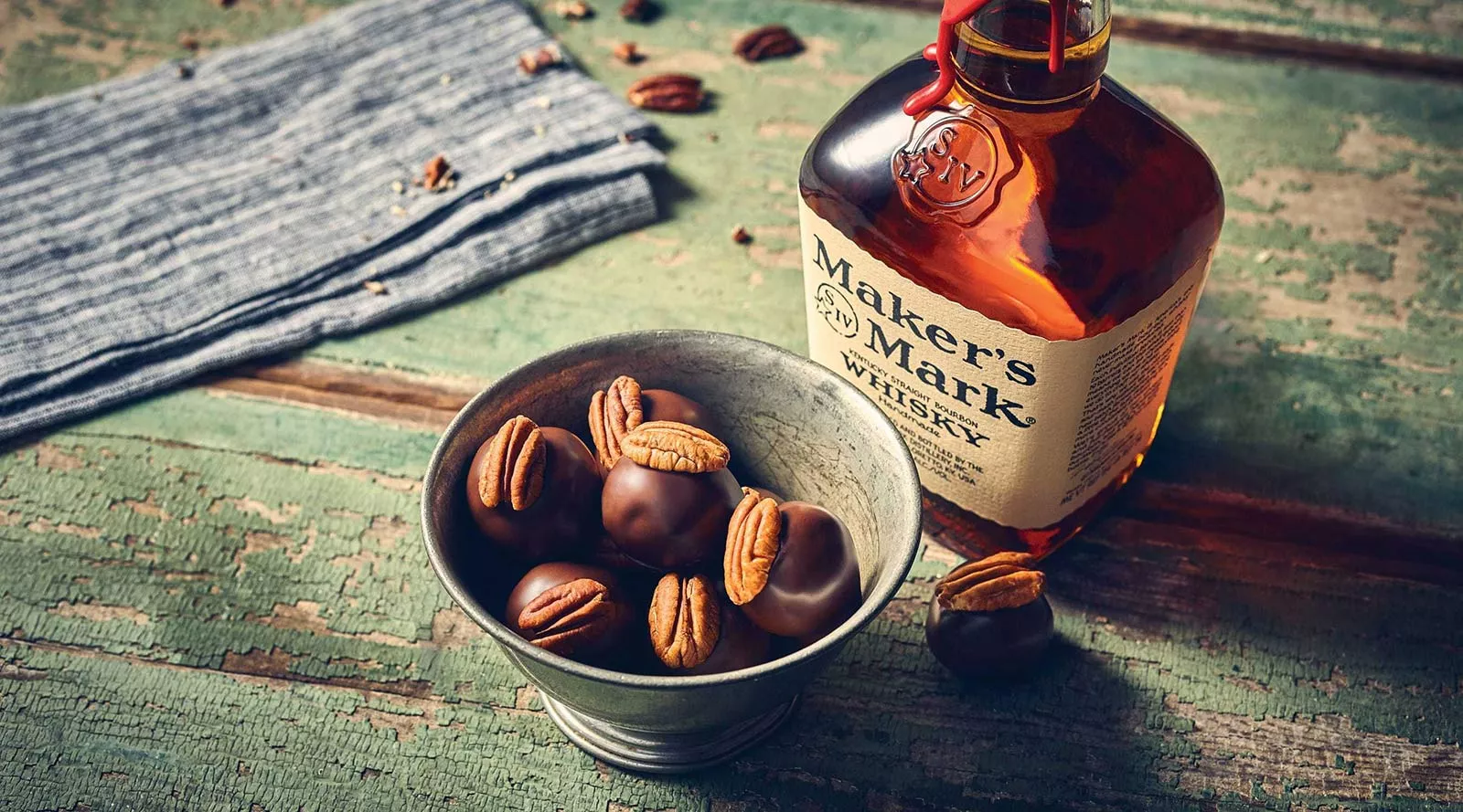 bourbon balls with pecans in metal bowl sitting on table next to a bottle of Maker's Mark