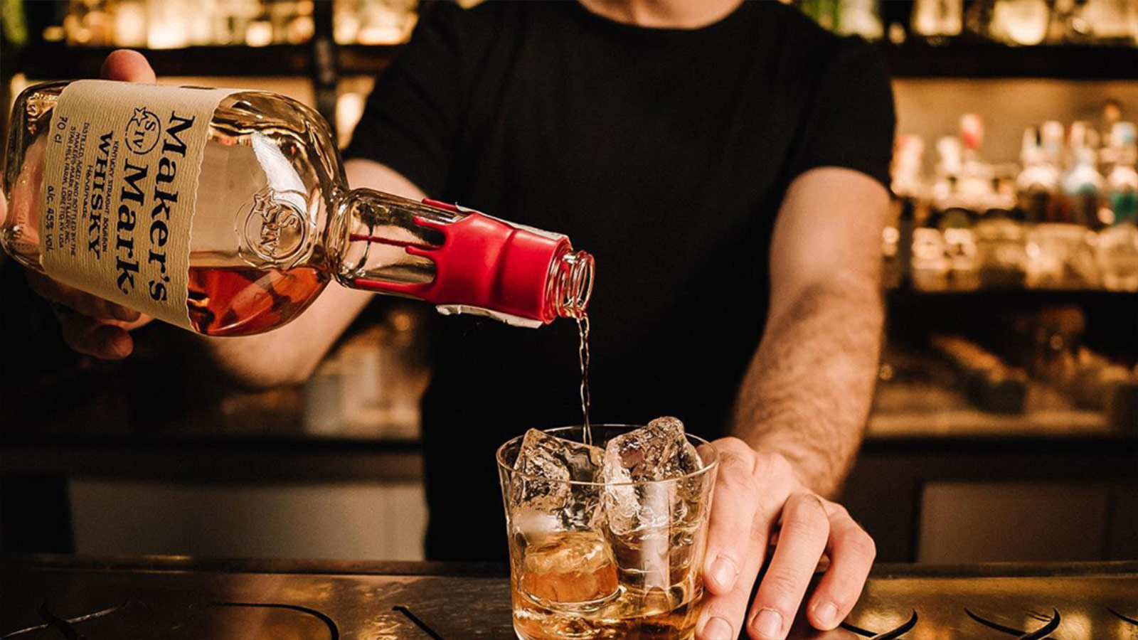A bartender pours Whisky Maker's Mark from a bottle into a glass with ice, Whisky Maker's Mark.