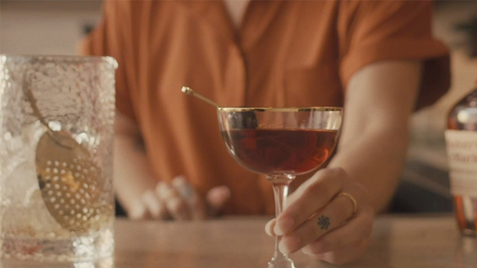 A bartender presents a garnished cocktail in a coupe glass, Whisky Maker's Mark.