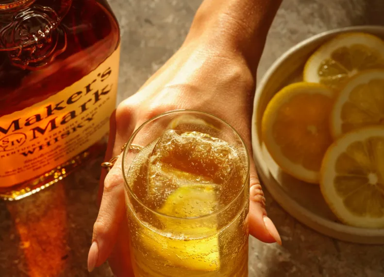 Man holding a glass filled with sour highball cocktail, with a bottle of this cocktail placed alongside.