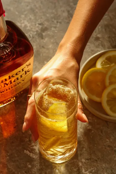 Man holding a glass filled with sour highball cocktail, with a bottle of this cocktail placed alongside.