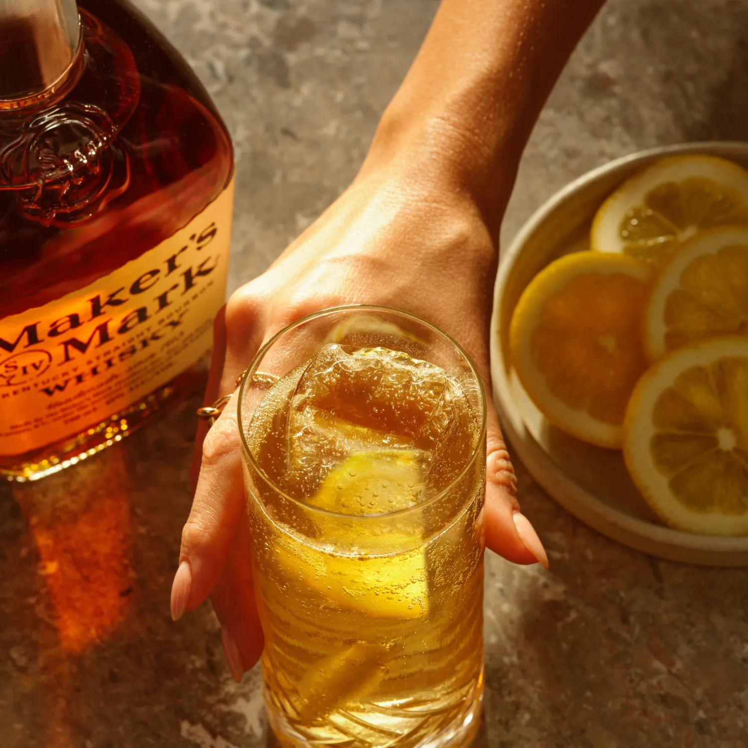 Man holding a glass filled with sour highball cocktail, with a bottle of this cocktail placed alongside.