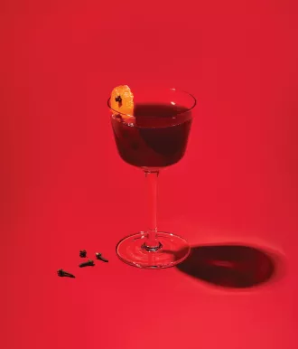 fireside Manhattan cocktail with garnishes in front of a red background