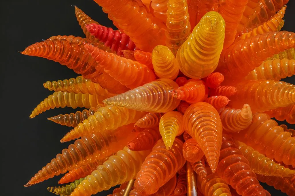 A vibrant glass sculpture featuring spiraled forms in shades of orange and yellow, resembling a fiery, abstract sea creature.