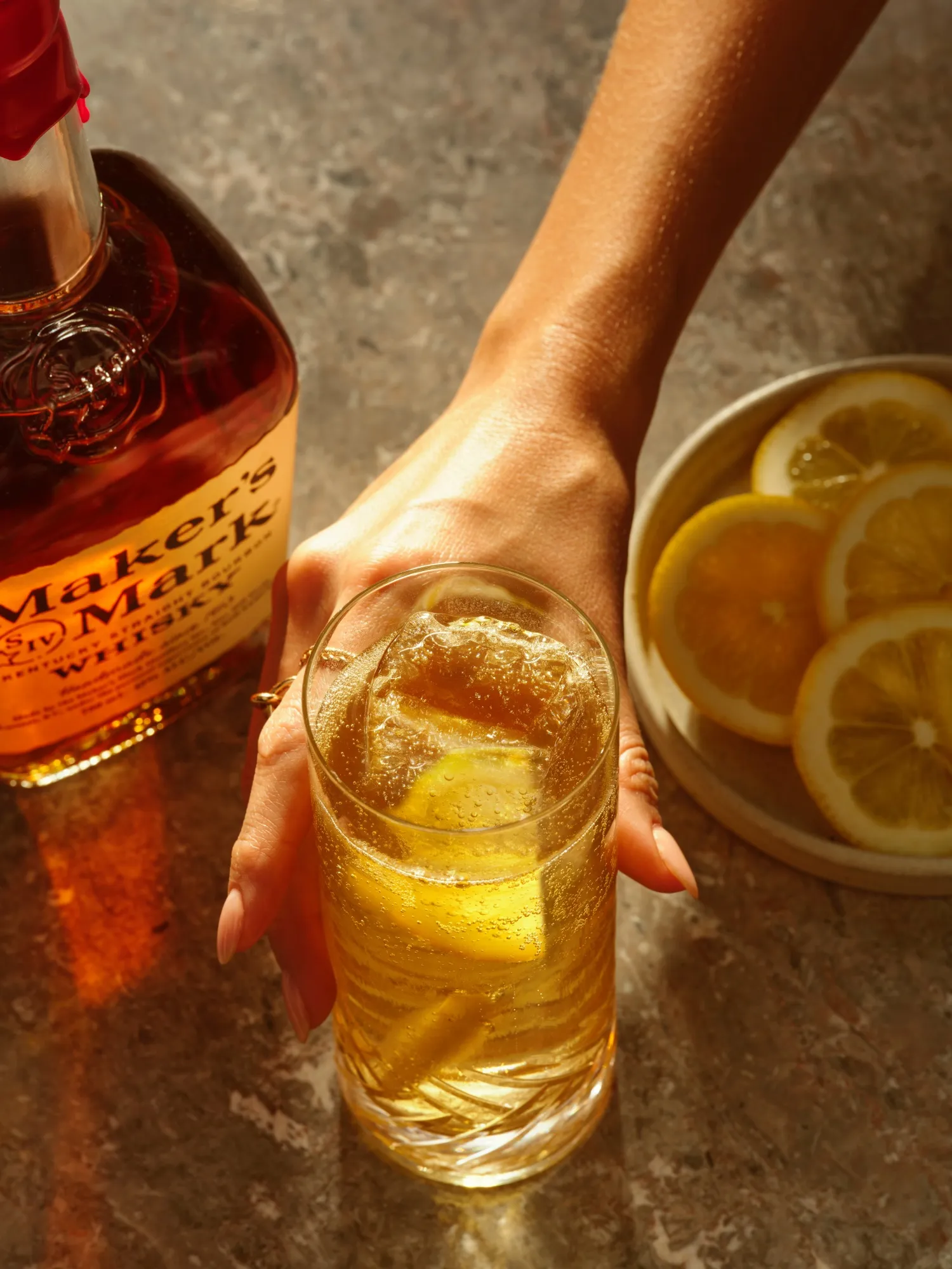 Man holding a glass filled with sour highball cocktail, with a bottle of this cocktail placed alongside.