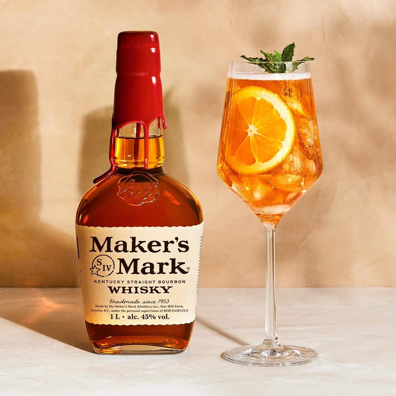A tall glass of Bourbon Spritz with an orange slice and mint garnish next to a bottle of Whisky Maker's Mark, Cocktail Whisky Maker's Mark.