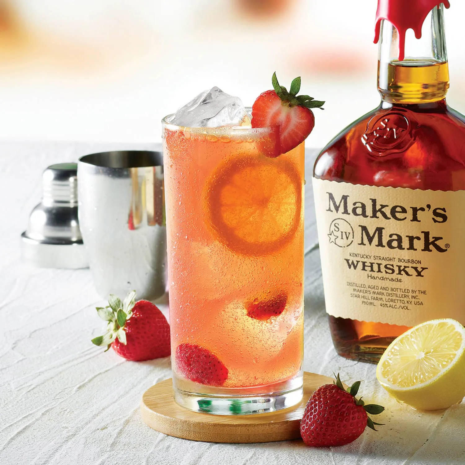 Kentucky Buck cocktail in a tall glass garnished with strawberries and an orange slice, next to a bottle of Whisky Maker's Mark, Cocktail Whisky Maker's Mark.