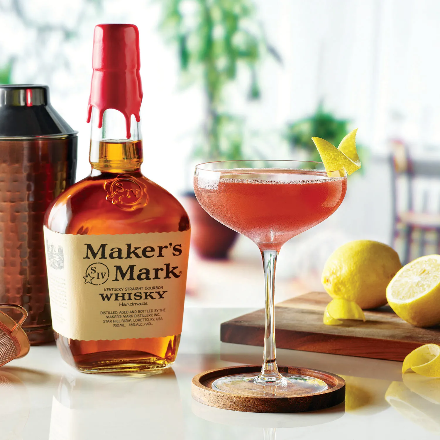 Paper Plane cocktail in a coupe glass next to a bottle of Maker's Mark and lemons, Cocktail Whisky Maker's Mark.