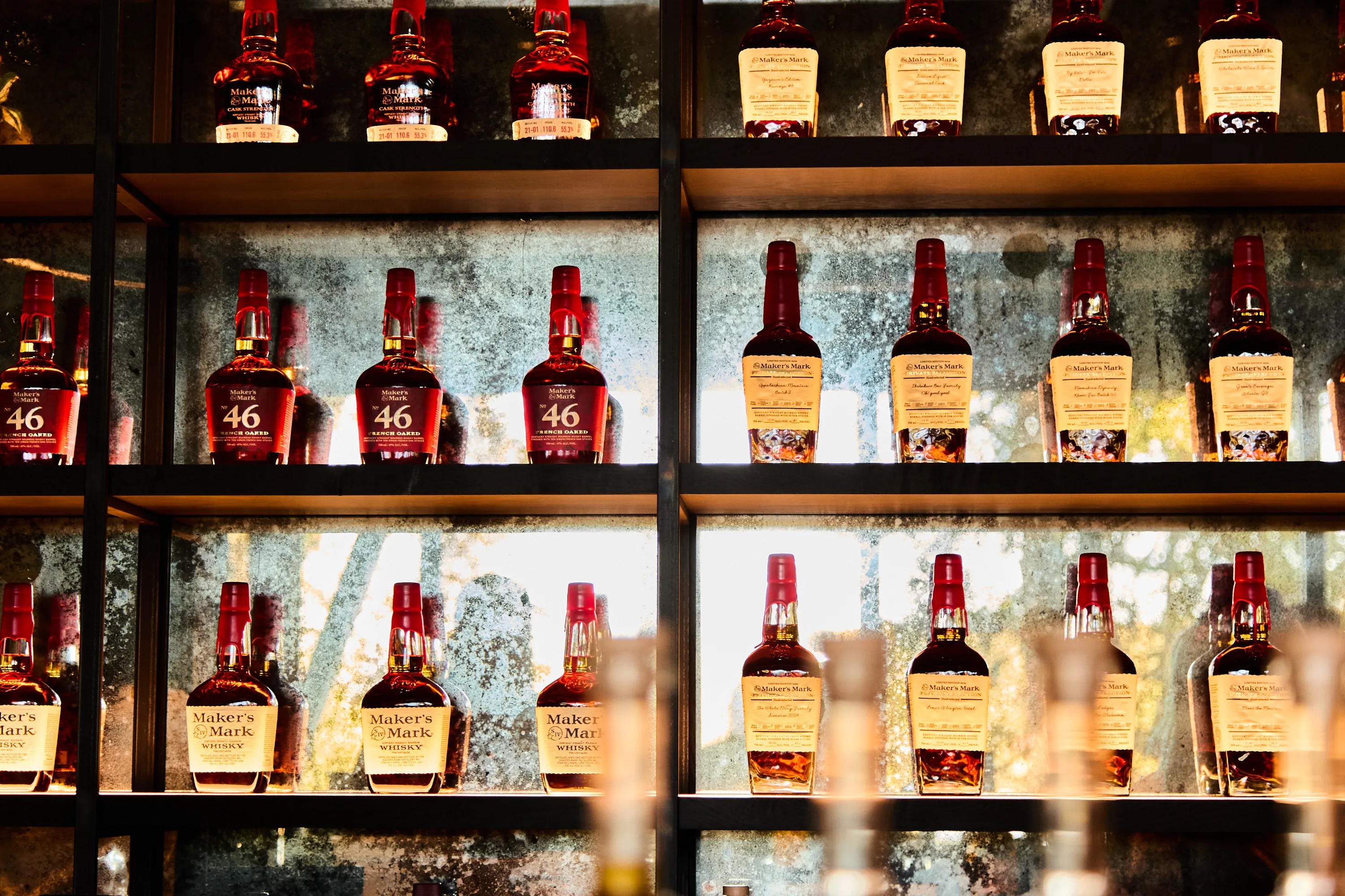 Shelves of Maker's Mark whiskey bottles displayed against a reflective glass background.