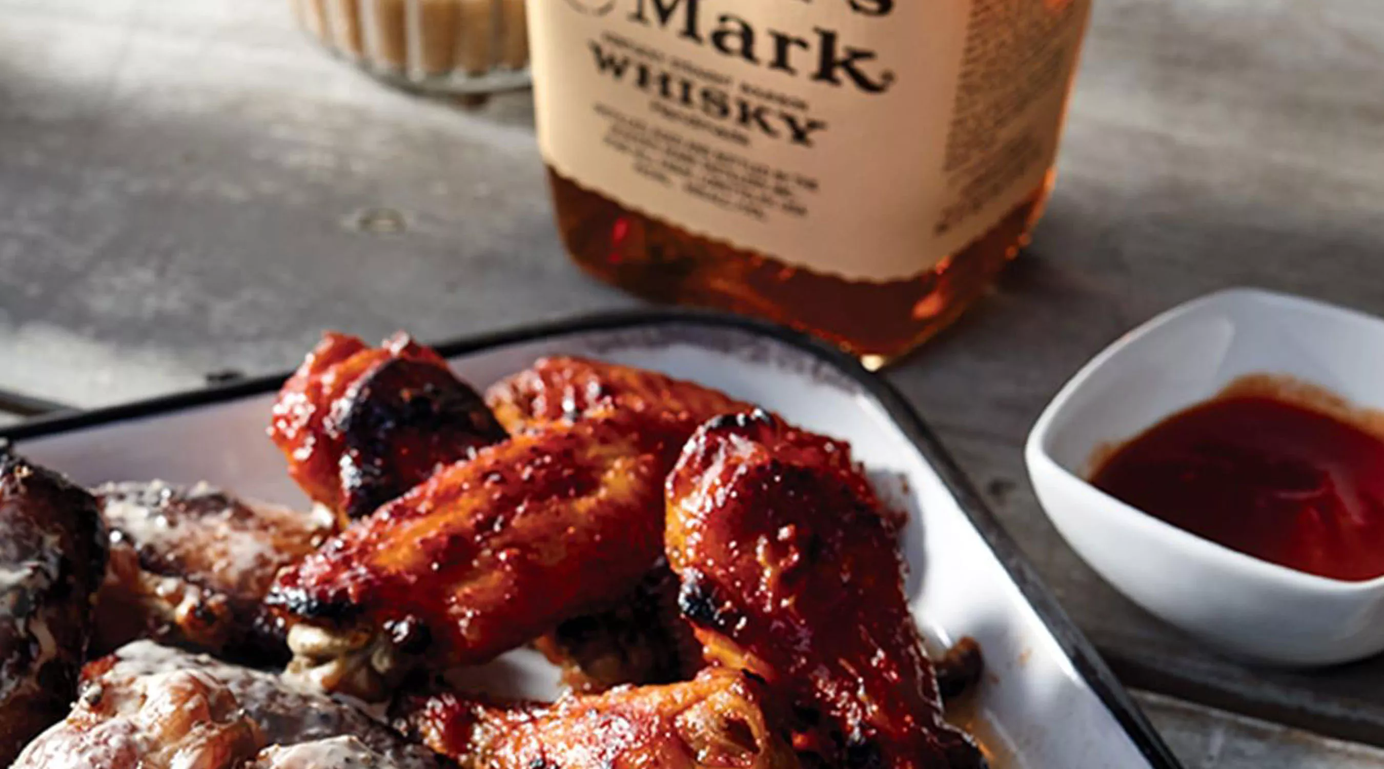 Baked chicken wings on a white platter next to a bottle of Maker's Mark.