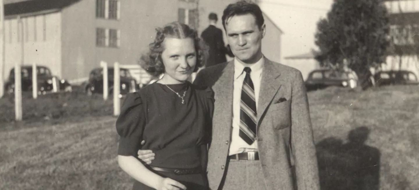 A black and white photo of the Maker's Mark founders, Margie and Bill Samuels. Margie is on the left in a dark dress, and Bill is on the right in a light suit and tie with his arm around her waist. 