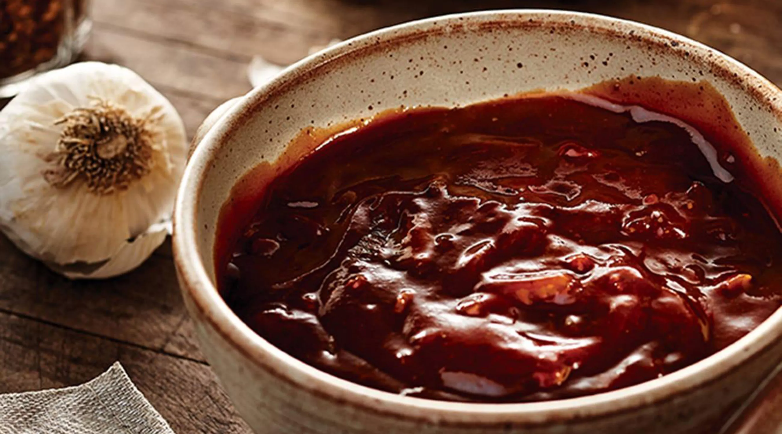 An image of bowl of barbeque sauce with a whole garlic bulb.
