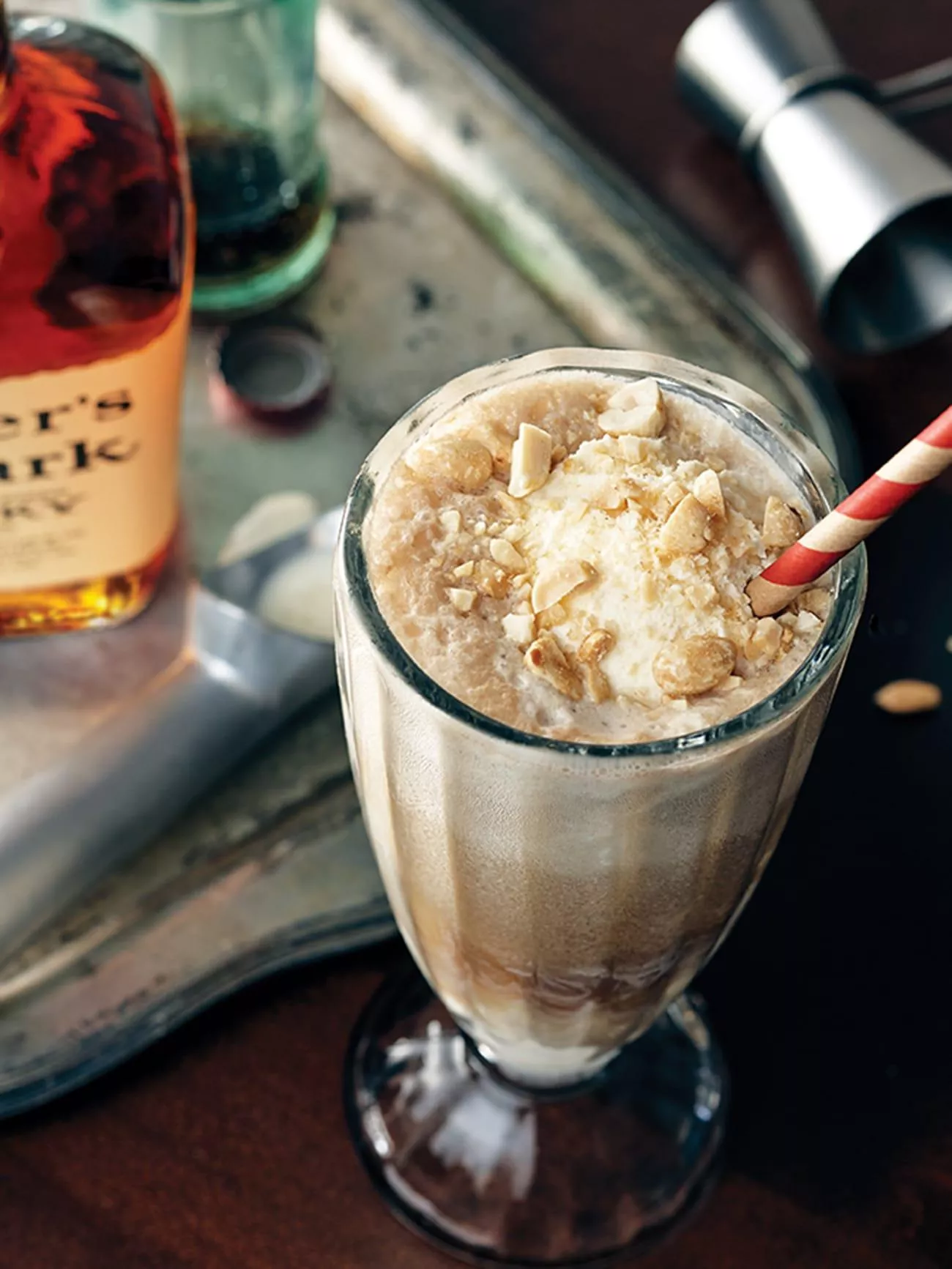 A top down image of a fountain style drink mixed with ice cream and Coca Cola with a red and white straw next to a bottle of classic Maker's Mark. 