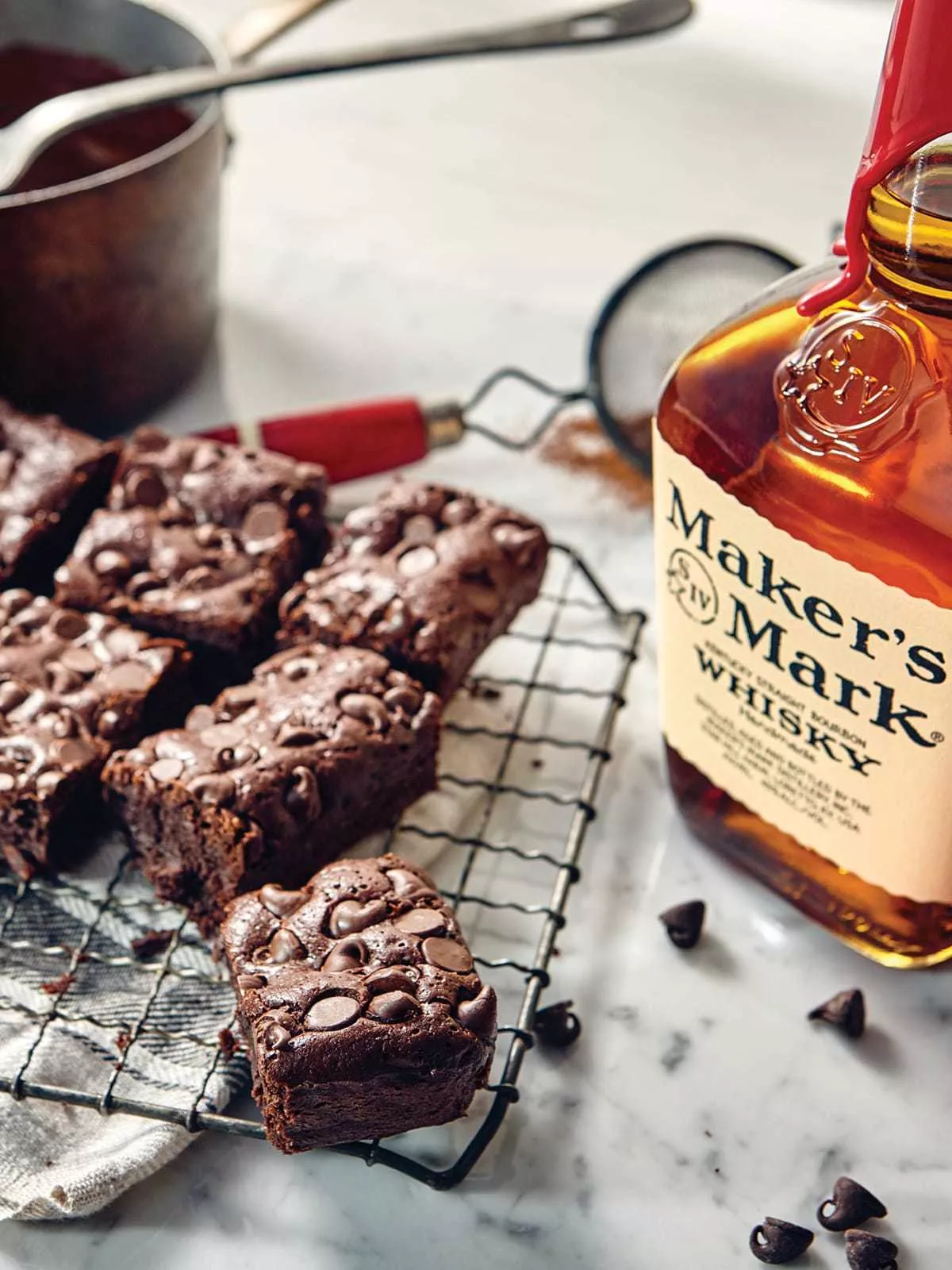 Brownies rest on a cooling rack cut into squares next to a bottle of Classic Maker's Mark.