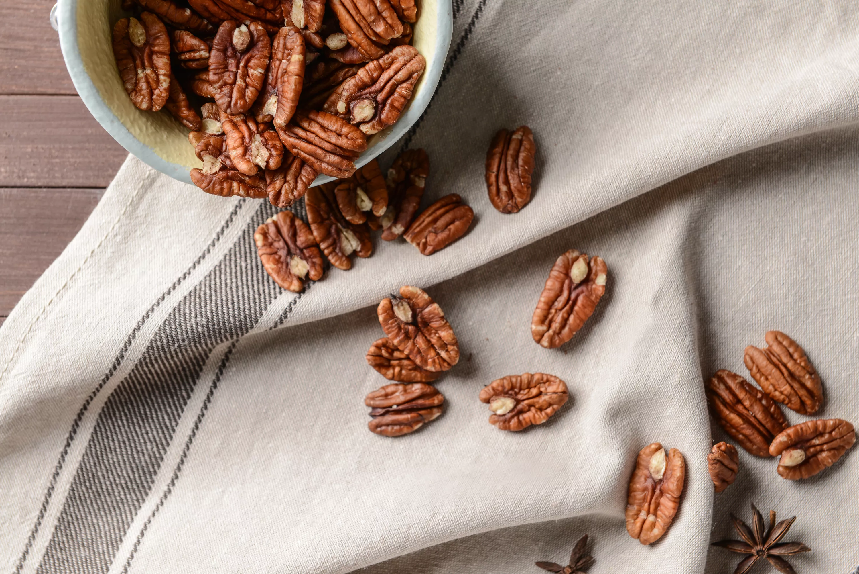 Pecans spill out of a small bowl onto a picnic napkin.