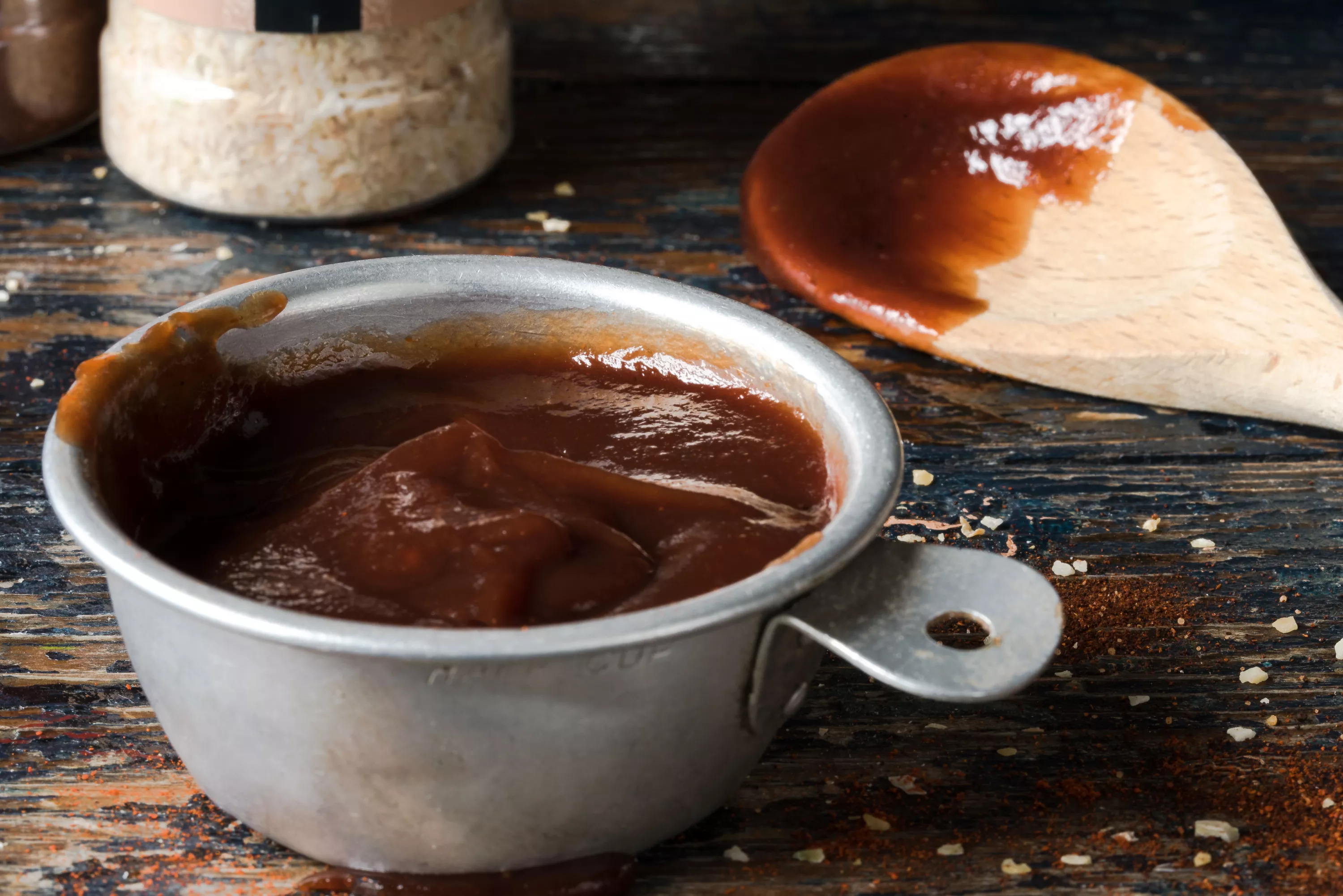 A ramekin of barbeque sauce next to a wooden spatula used to stir it.