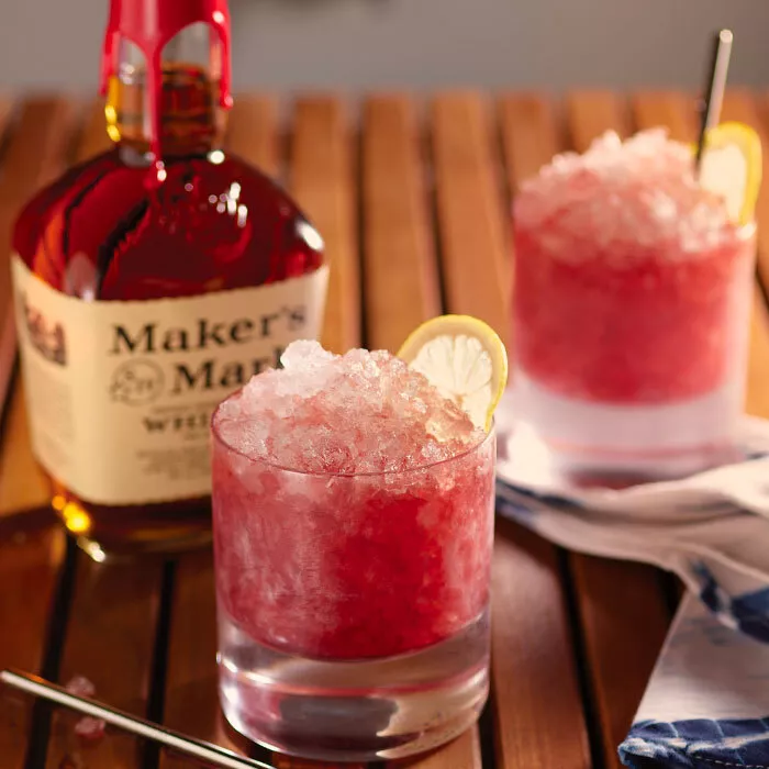 Two tumblers with ice and the Maker's Mark Bourbon Renewal cocktail with a lemon garnish on a tray sit next to a bottle of Maker's Mark.