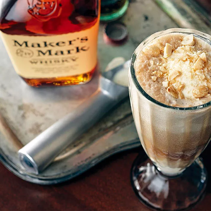 makers mark cola float in tall glass on table next to a bottle of makers mark bourbon