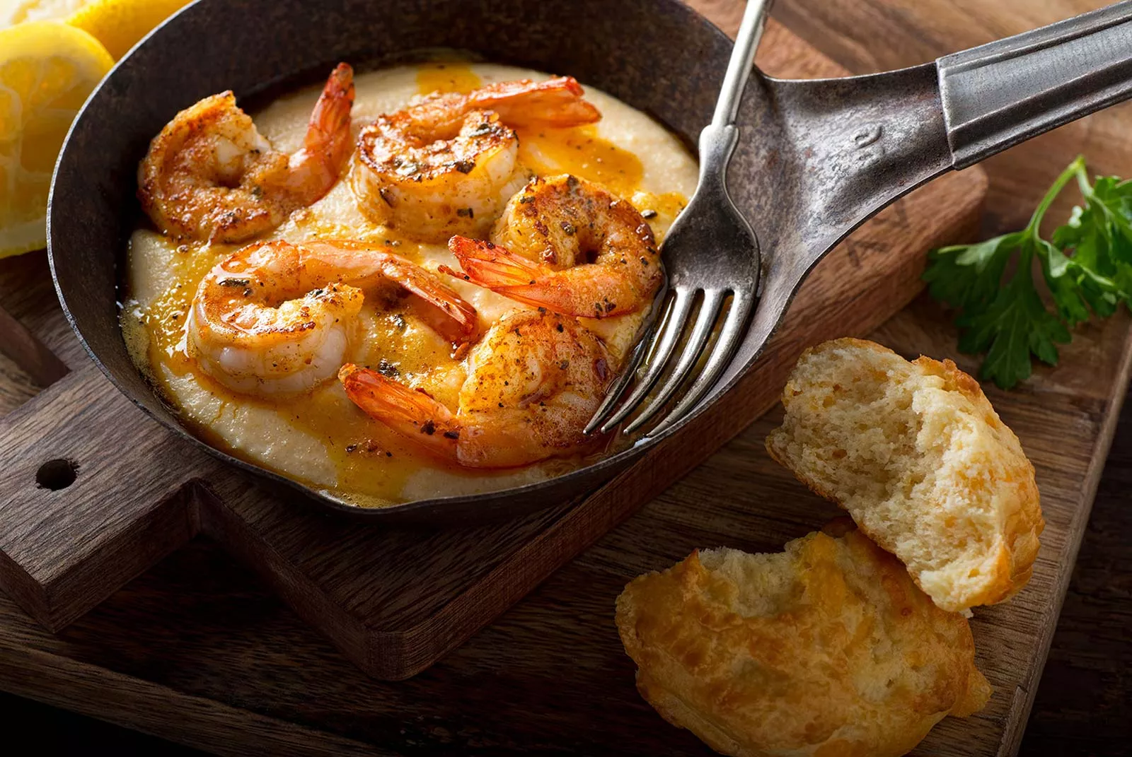 The final recipe of cooked shrimp in a small skillet with a fork and lemon wedge.